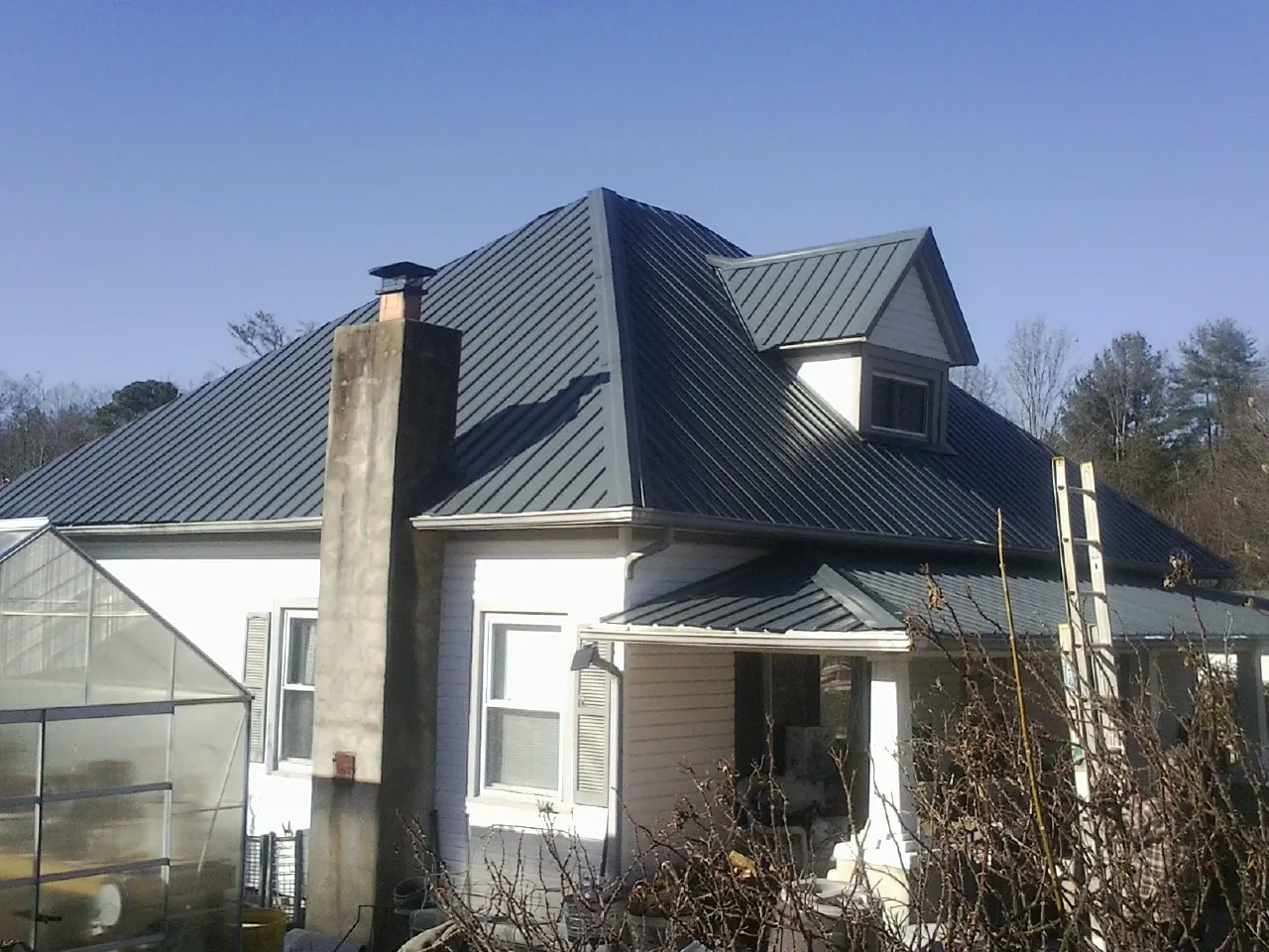 Dark blue standing seam metal roof on a white farmhouse with dormer — Slate & Tile Roof Repair by Roofing Brothers in Avonmore