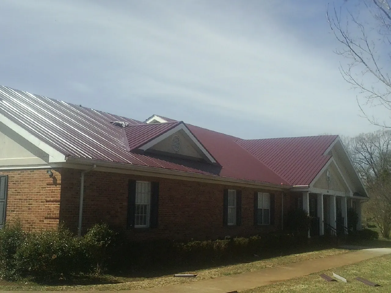 Red metal roof with gabled entries on a long brick building, from a Hail Damage Roof Repair job in Avonmore