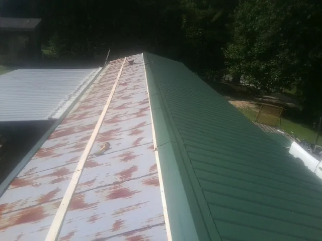 Old rusted panels beside newly installed green metal roofing — Wind Damage Roof Repair by Roofing Brothers in Avonmore