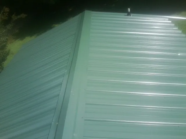 New green metal panels meeting at the ridge of a roof — Flat Roof Repair work by our crew in Avonmore