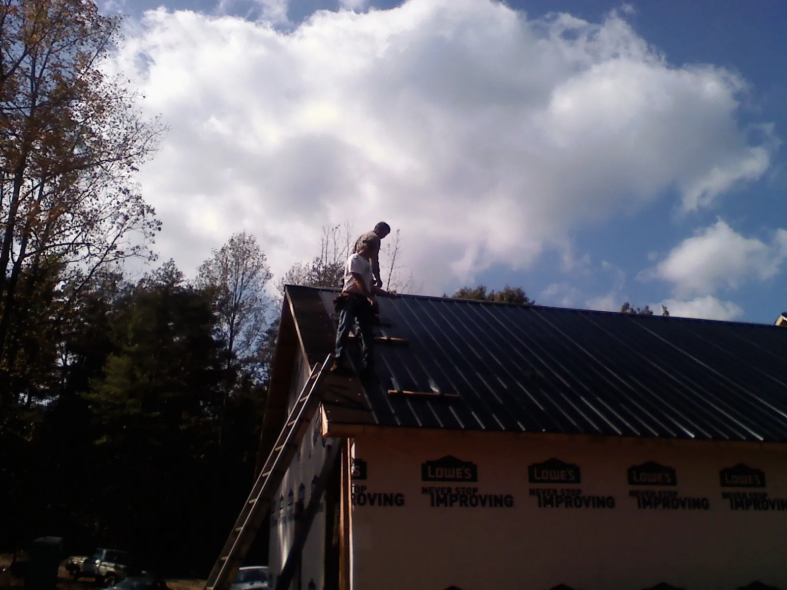 Roofer fastening dark metal panels high against a cloudy sky, from a Roof Inspection job in Avonmore