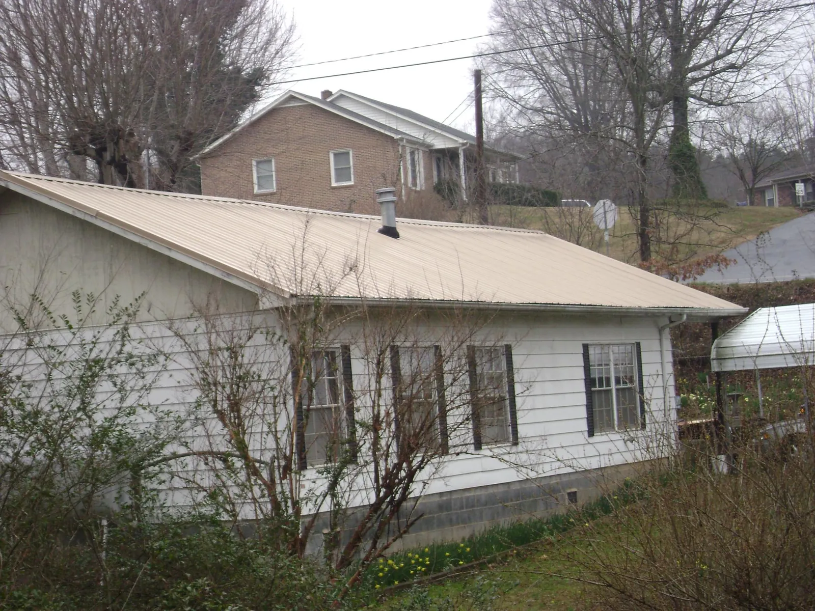 Tan metal roof on a white sided house set into a hillside — Commercial Roofing by Roofing Brothers in Avonmore