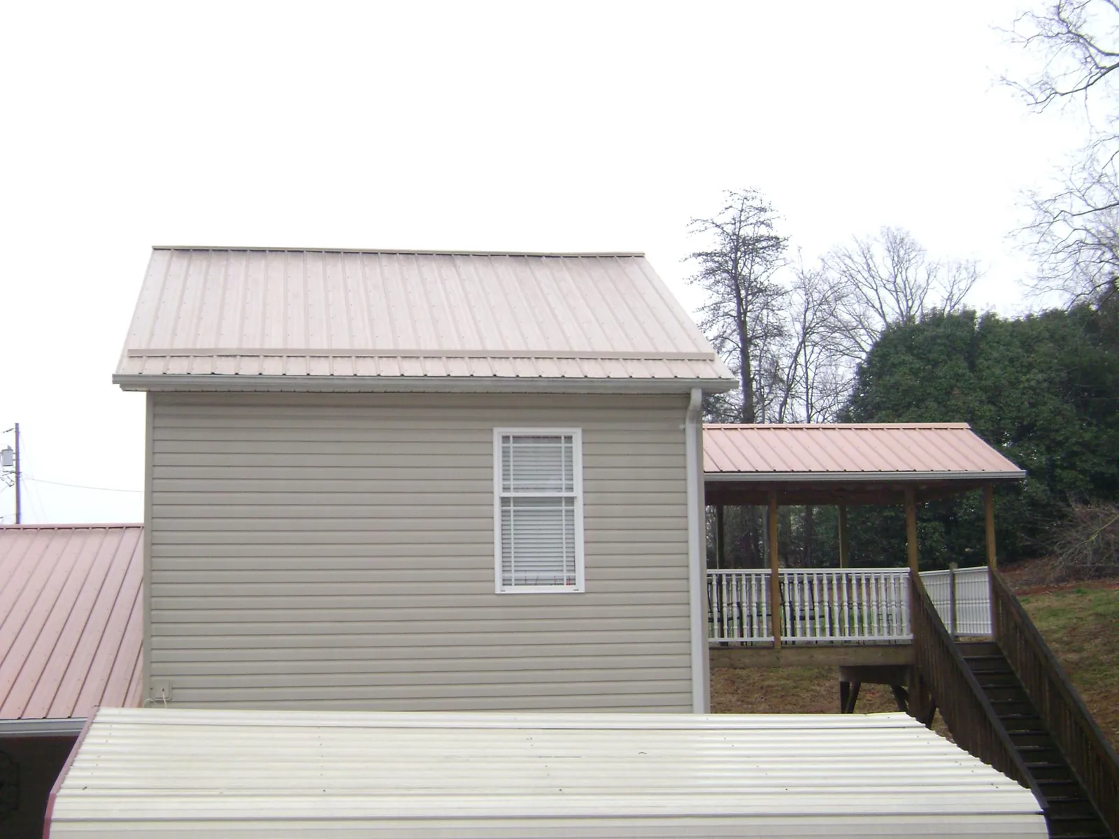 Tan metal roofs on a two story addition and attached porch, from a Roof Replacement job in Avonmore